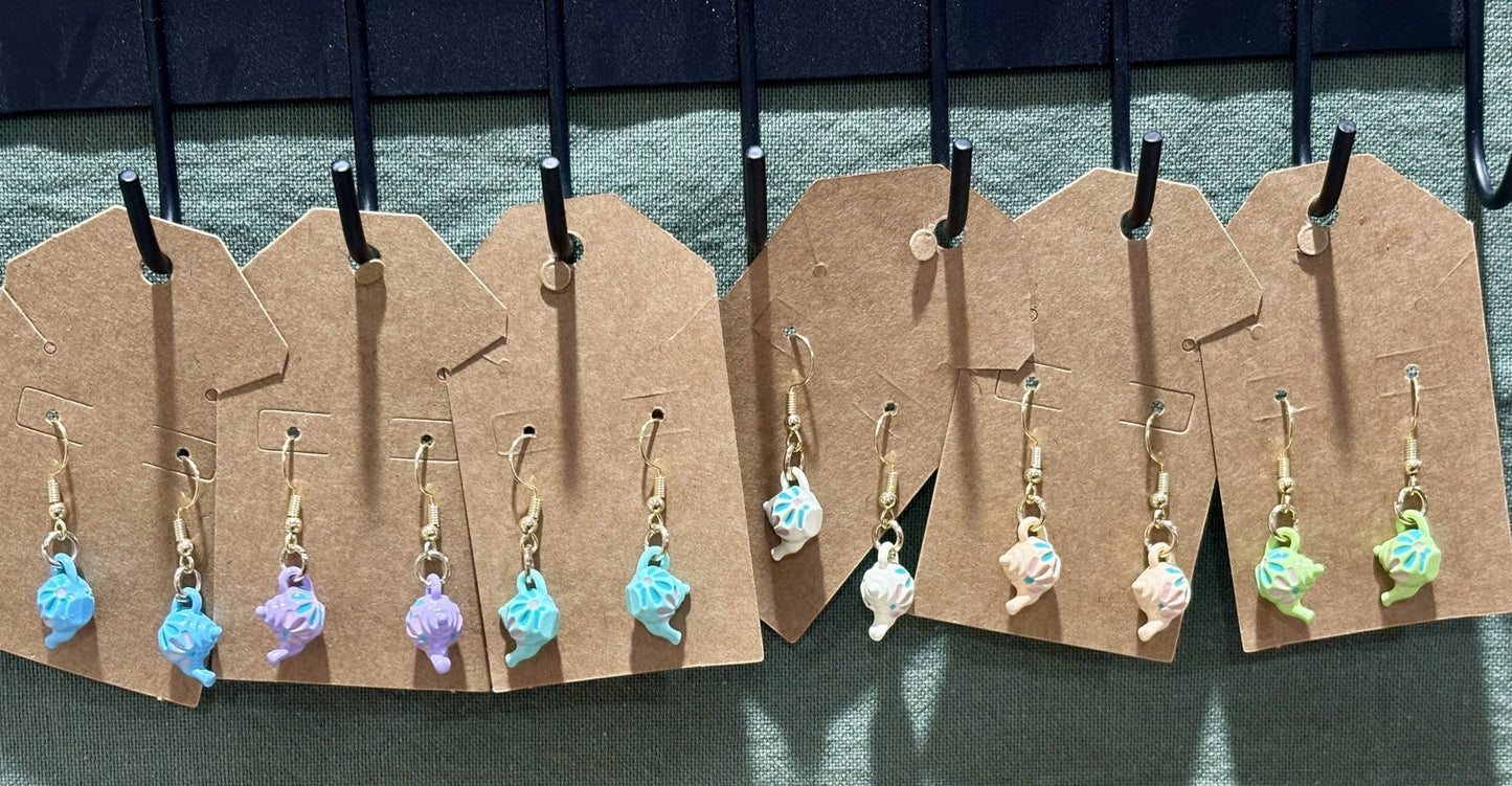 Patrick and Penn miniature teapot dangle earrings in various pastel colors with gold-tone hooks on display cards.