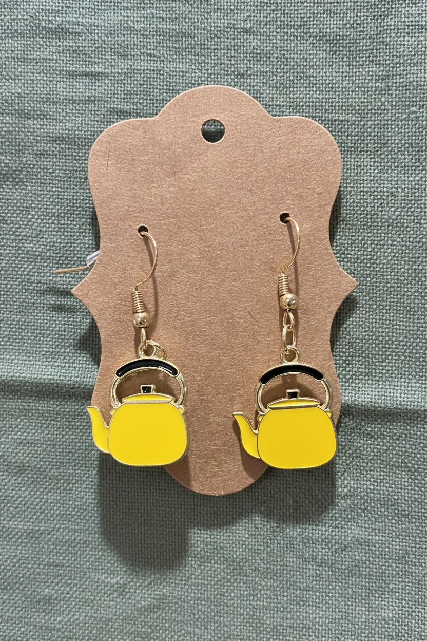Yellow teapot-shaped earrings on a brown card against a gray background