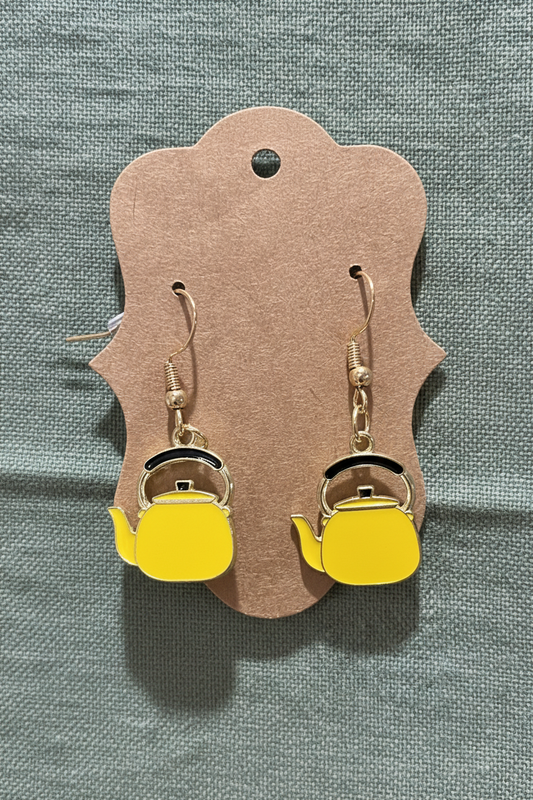 Yellow teapot-shaped earrings on a brown card against a gray background